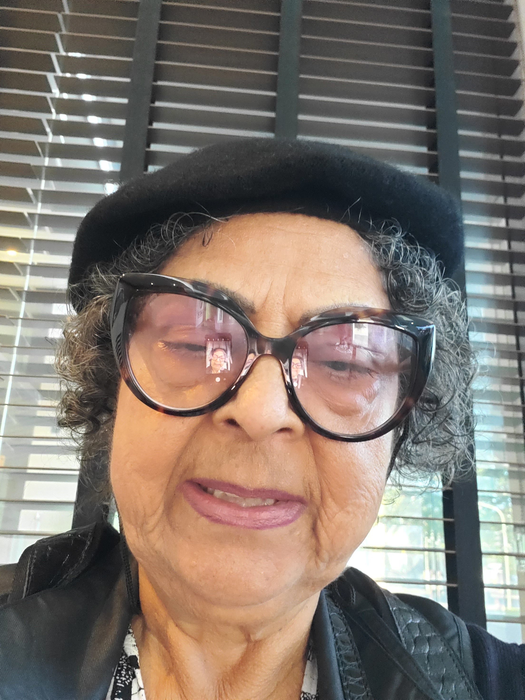 Uma linda mulher de boina preta e sorrindo usando óculos. Eu Bel Talarico